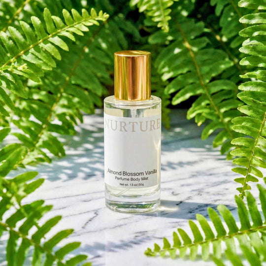 Bottle of NURTURE Almond Blossom Vanilla perfume body mist on a marble surface with fern leaves in the background