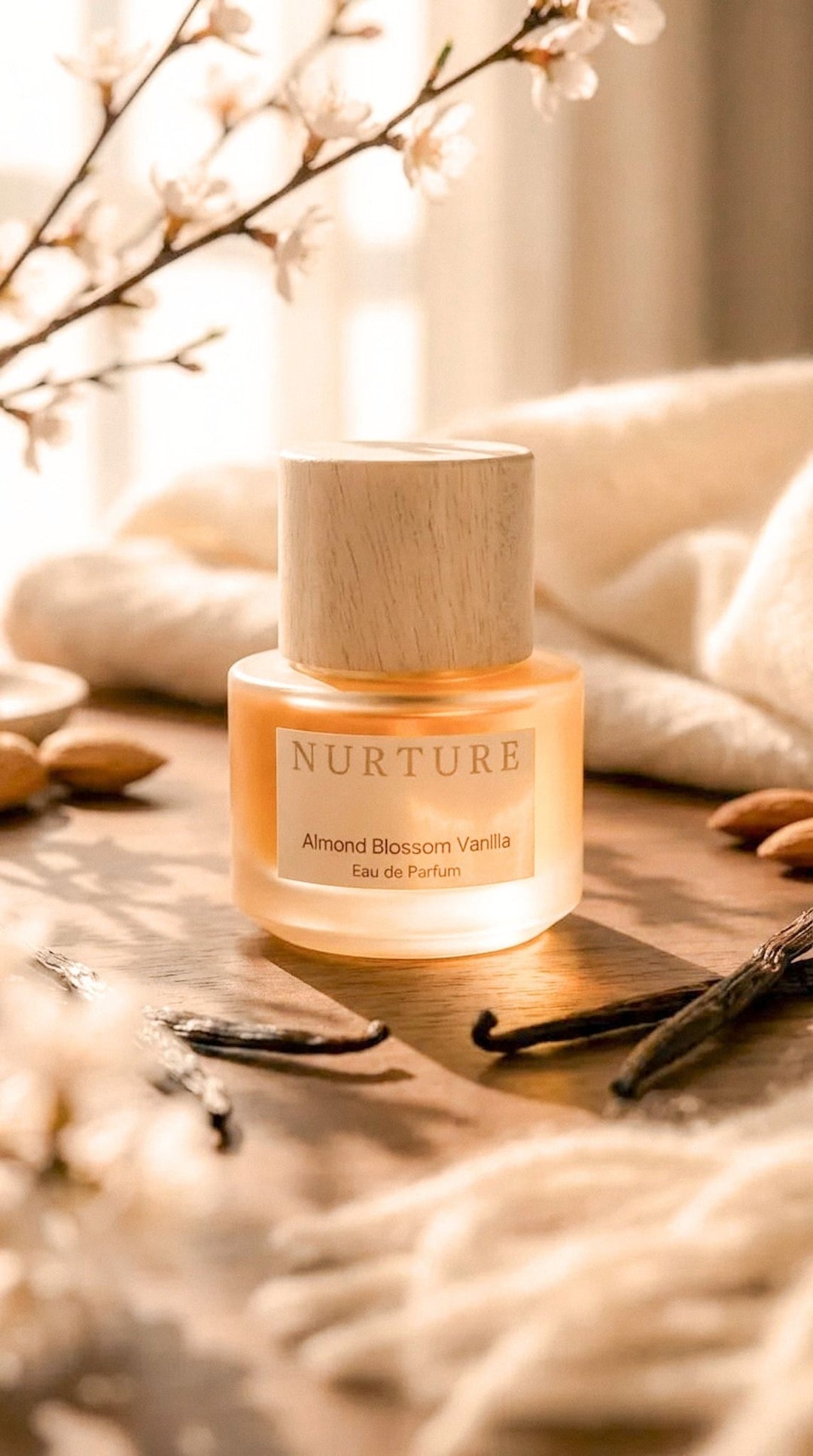 Perfume bottle labeled 'Nurture Almond Blossom Vanilla on a wooden surface with vanilla beans and flowers.