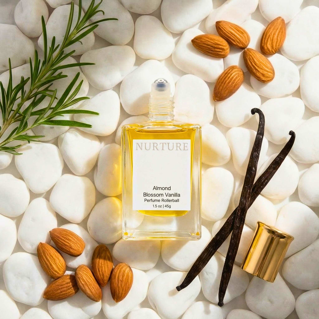 Bottle of Almond Blossom Vanilla rollerball on a bed of white pebbles with almonds and vanilla gourds.
