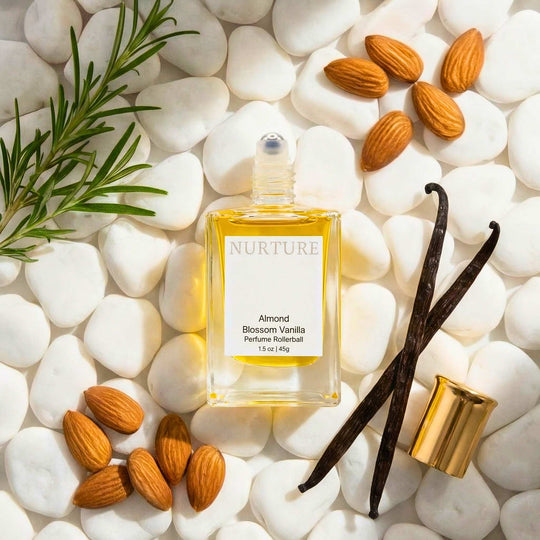 Bottle of Almond Blossom Vanilla rollerball on a bed of white pebbles with almonds and vanilla gourds.