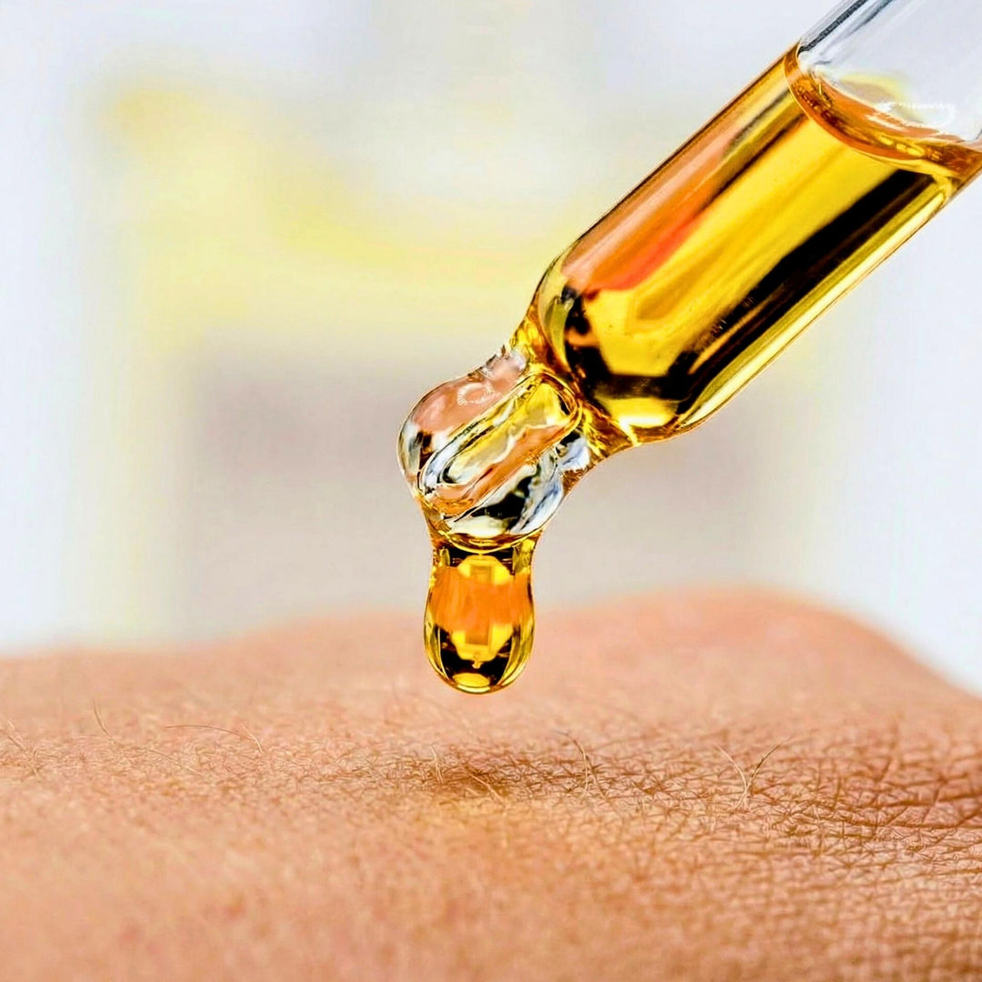 Gold-colored liquid being dripped onto skin from a dropper.