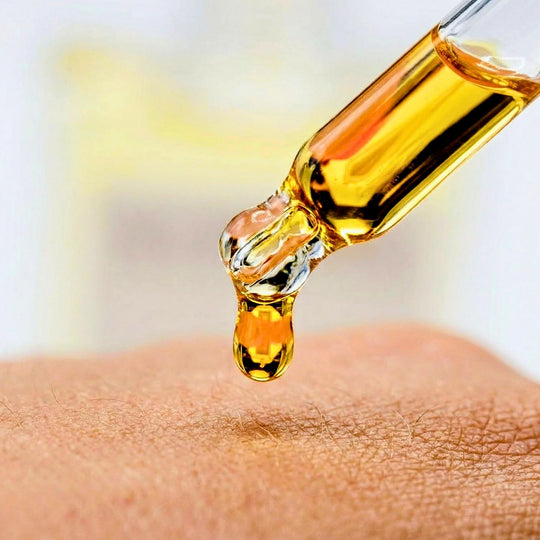 Gold-colored liquid being dripped onto skin from a dropper.