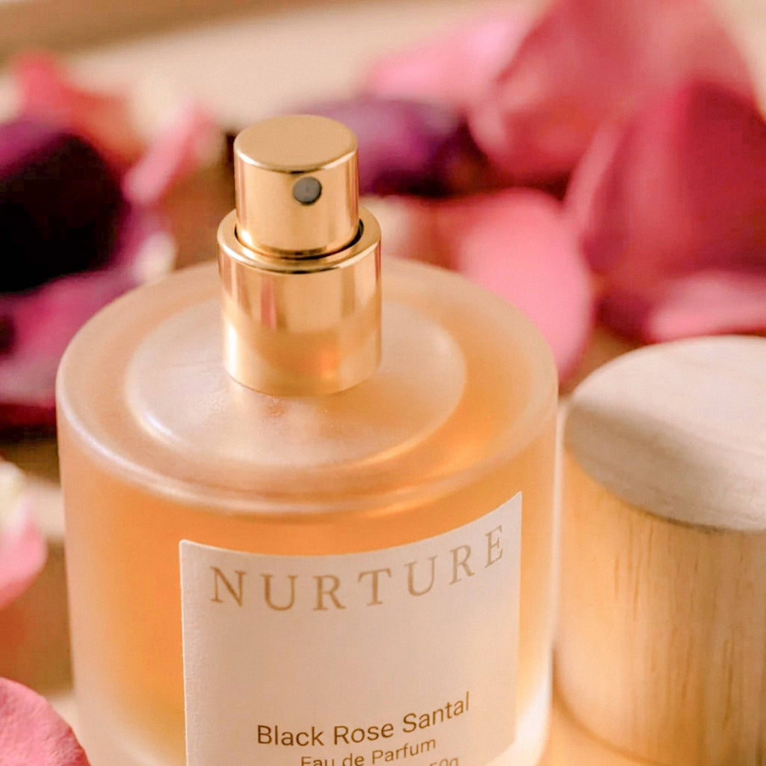 Black Rose Santal perfume with a gold cap, surrounded by pink flowers.