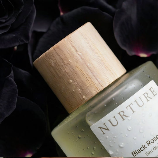Bottle of Nurture Black Rose Eau de Parfum with wooden cap on a bed of black rose petals.