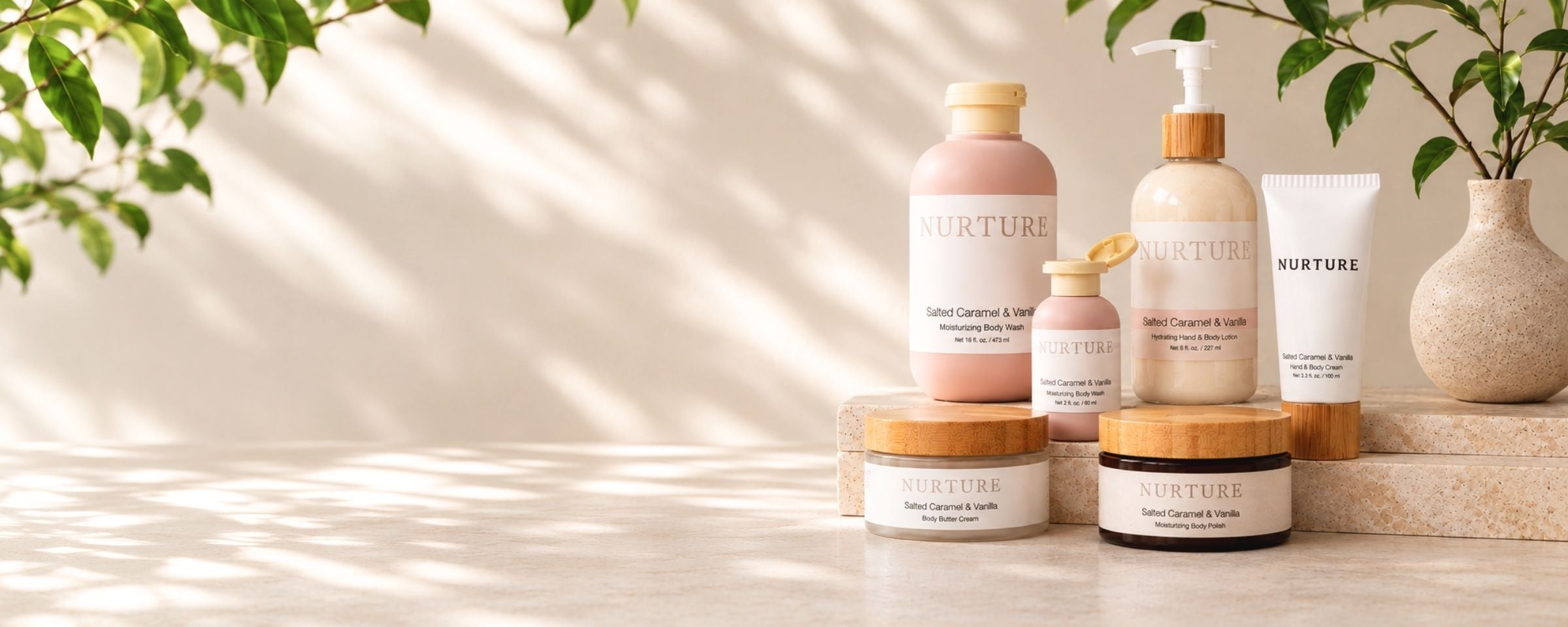 A set of NURTURE skincare products including a pump bottle, a tube, and jars with bamboo lids, arranged on a light stone surface with soft leaf shadows and a vase of greenery in the background.