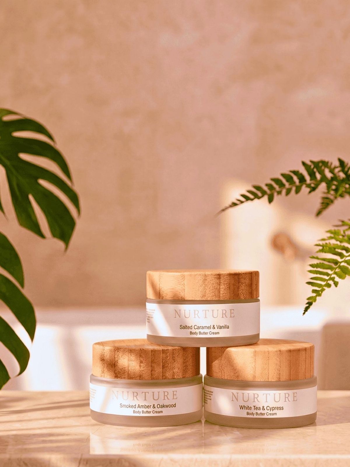 Three jars of 'Nurture' skincare products on a wooden surface with a blurred plant background.