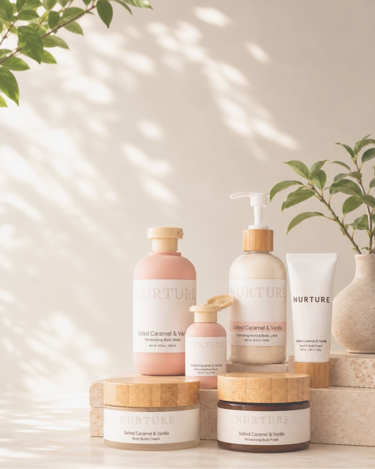 A set of six NURTURE body care products in soft pastel pink, beige, and white, arranged on wooden blocks with a neutral background and soft leaf shadows.