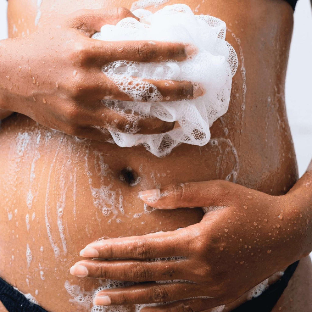 Woman scrubbing her belly with a shower sponge.