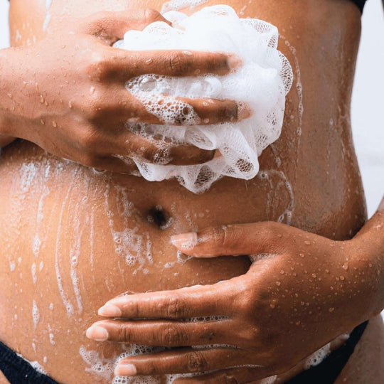 Woman scrubbing her belly with a shower sponge.