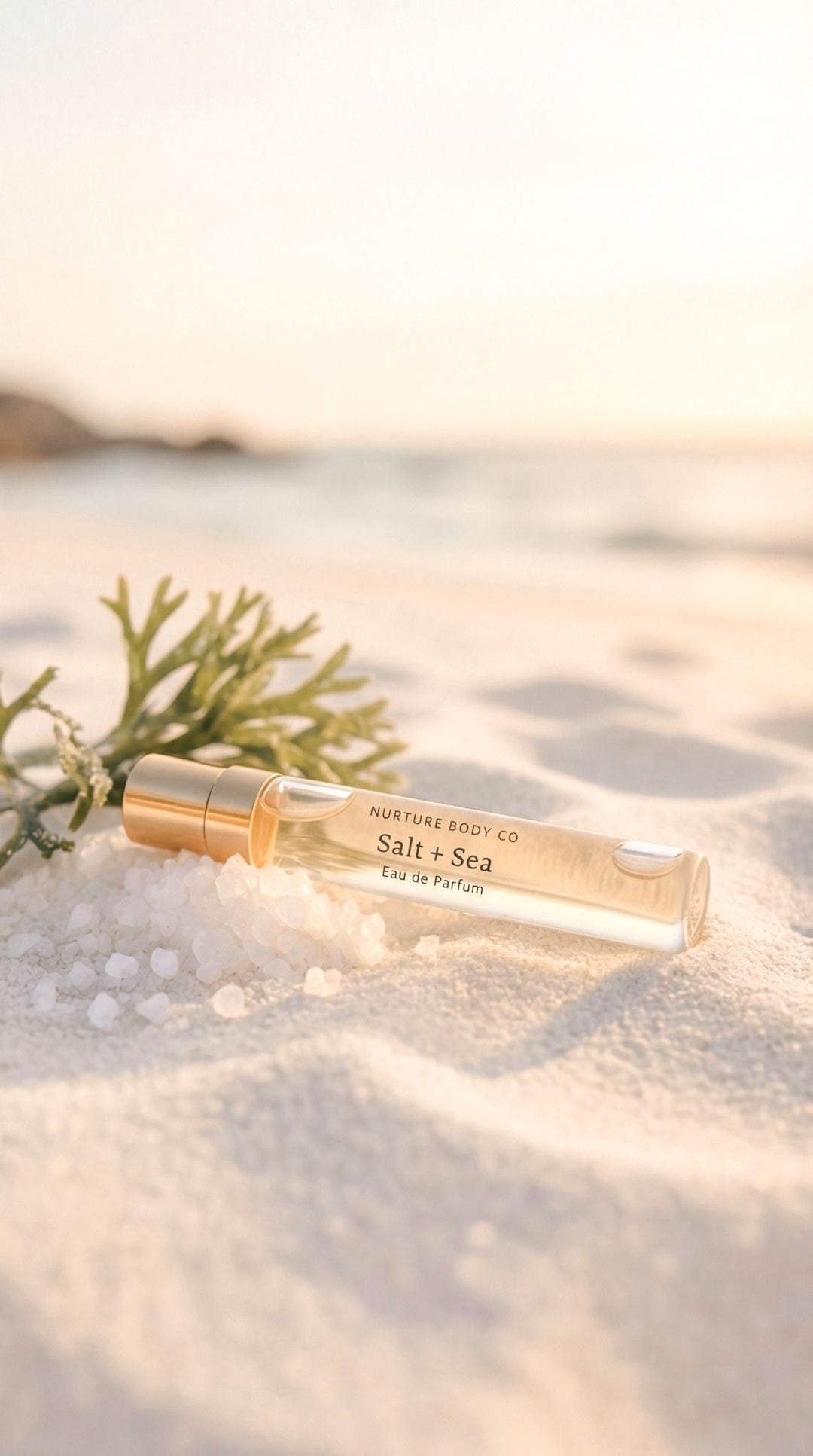 Roll-on perfume bottle labeled 'Salt + Sea' on sand with ocean background