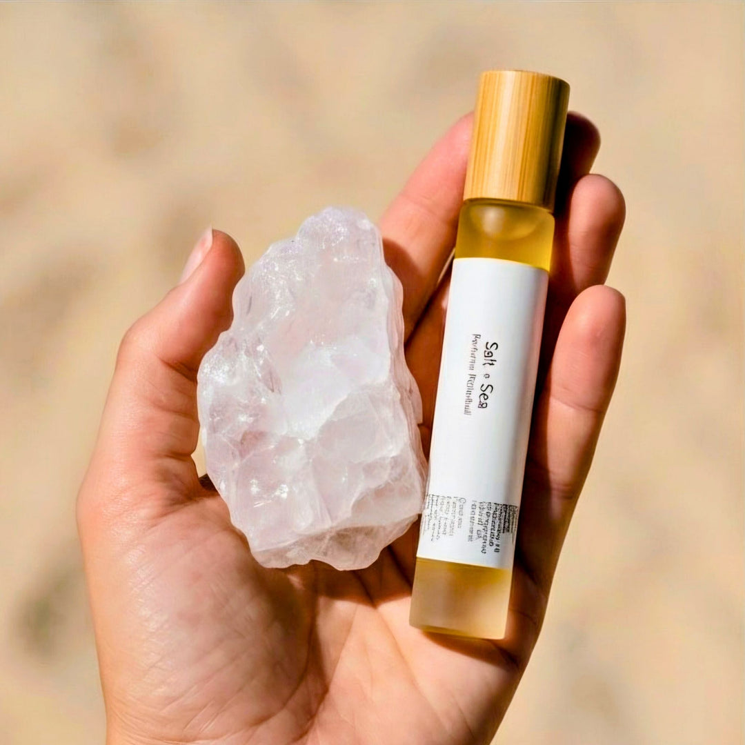 Hand holding a crystal and a small Salt + Sea perfume rollerball against a blurred natural background