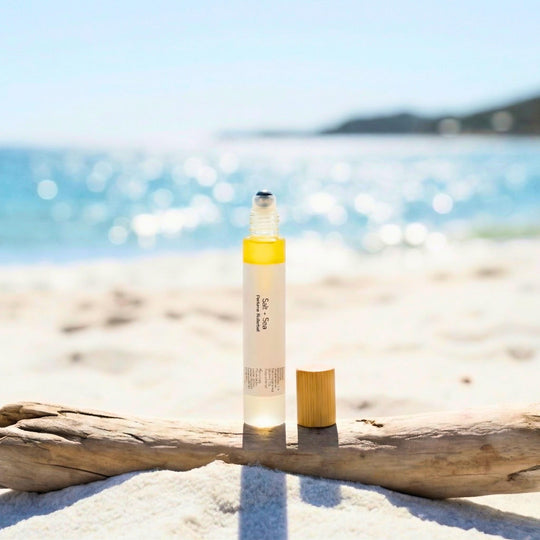 Salt + Sea perfume rollerball bottle on a piece of driftwood on the beach.