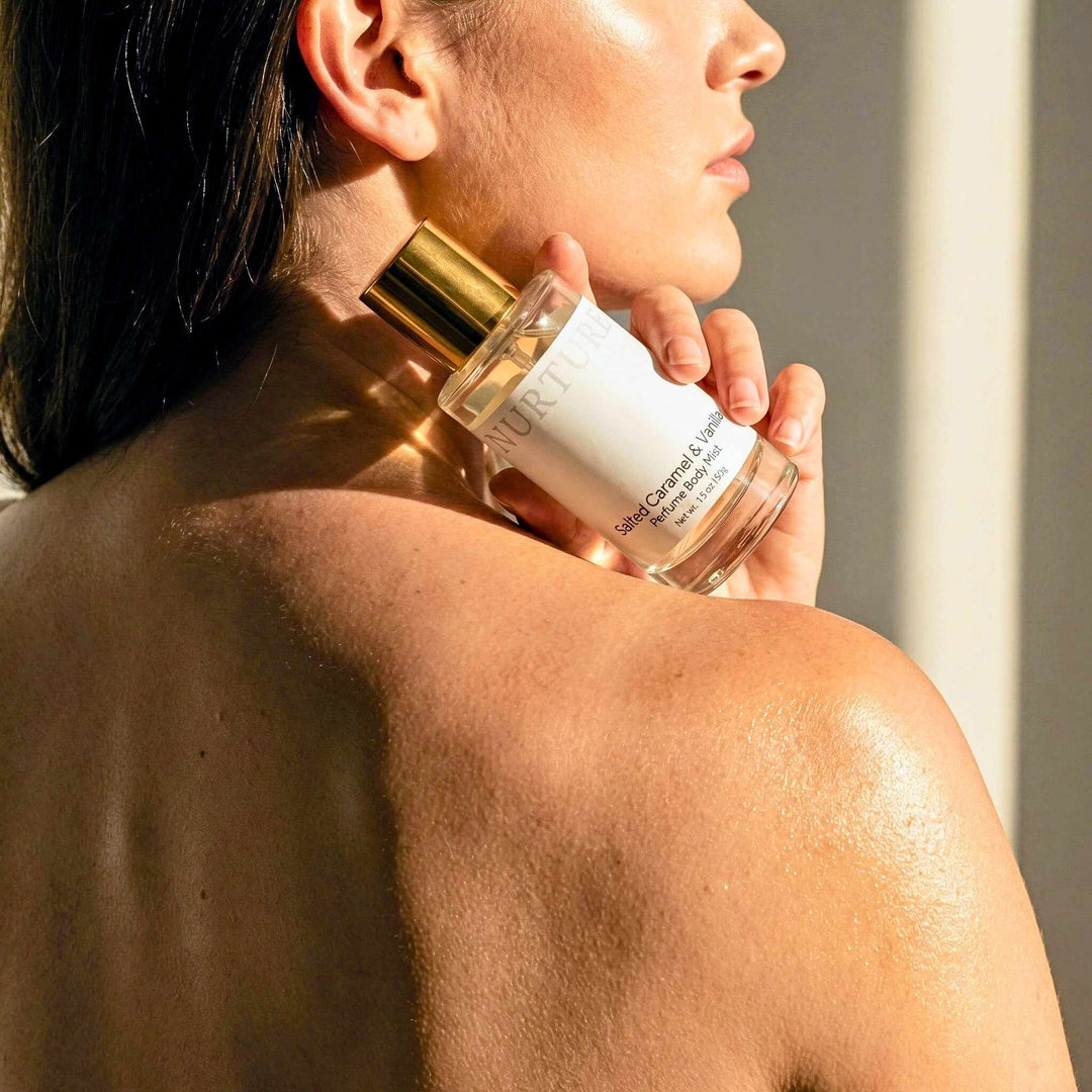 Woman holding a bottle of Salted Caramel Perfume Body Mist next to her shoulder.
