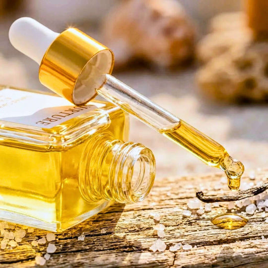 Gold dropper bottle with a droplet of oil on a wooden surface