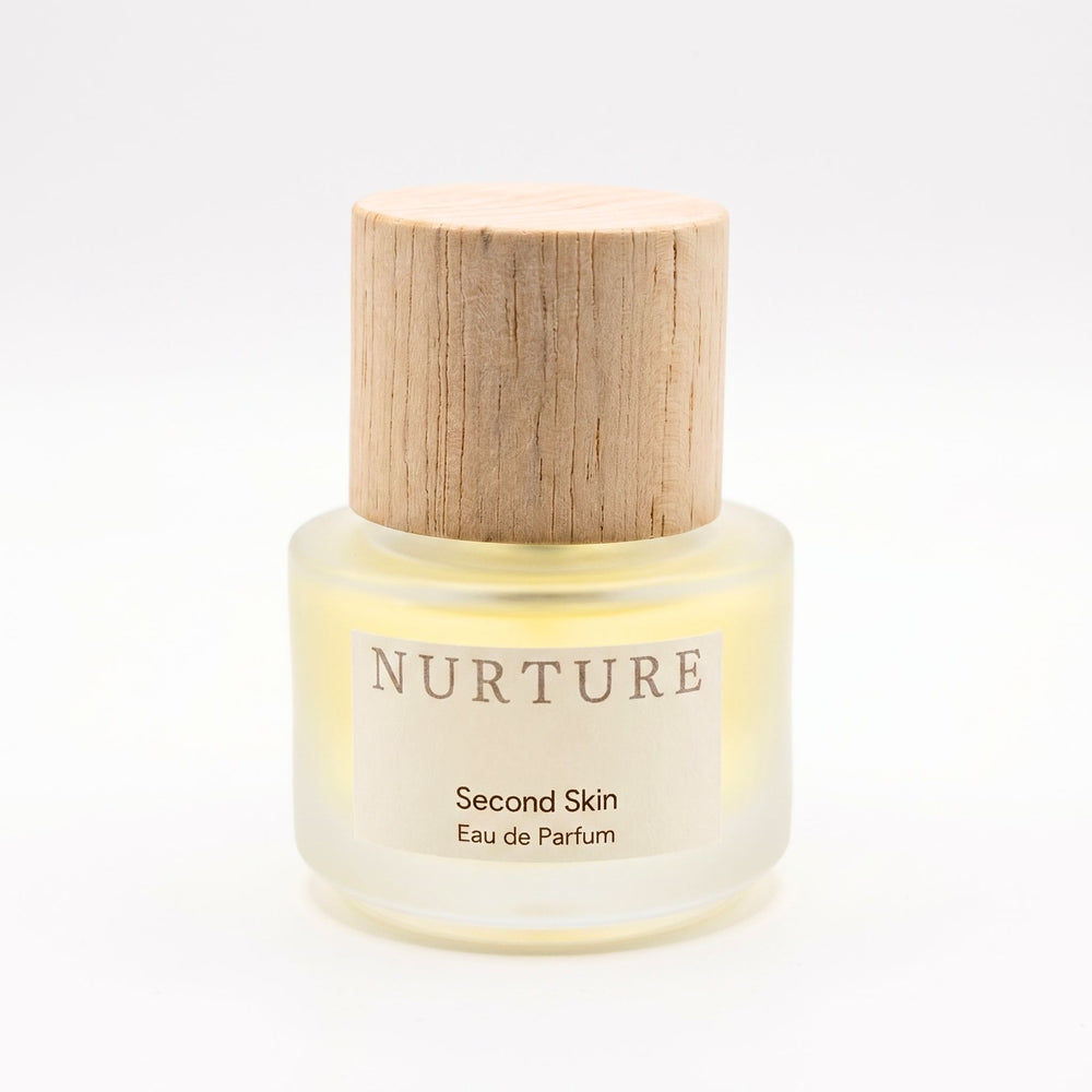 Perfume bottle labeled 'Nurture Second Skin Eau de Parfum' with wooden cap on a white background
