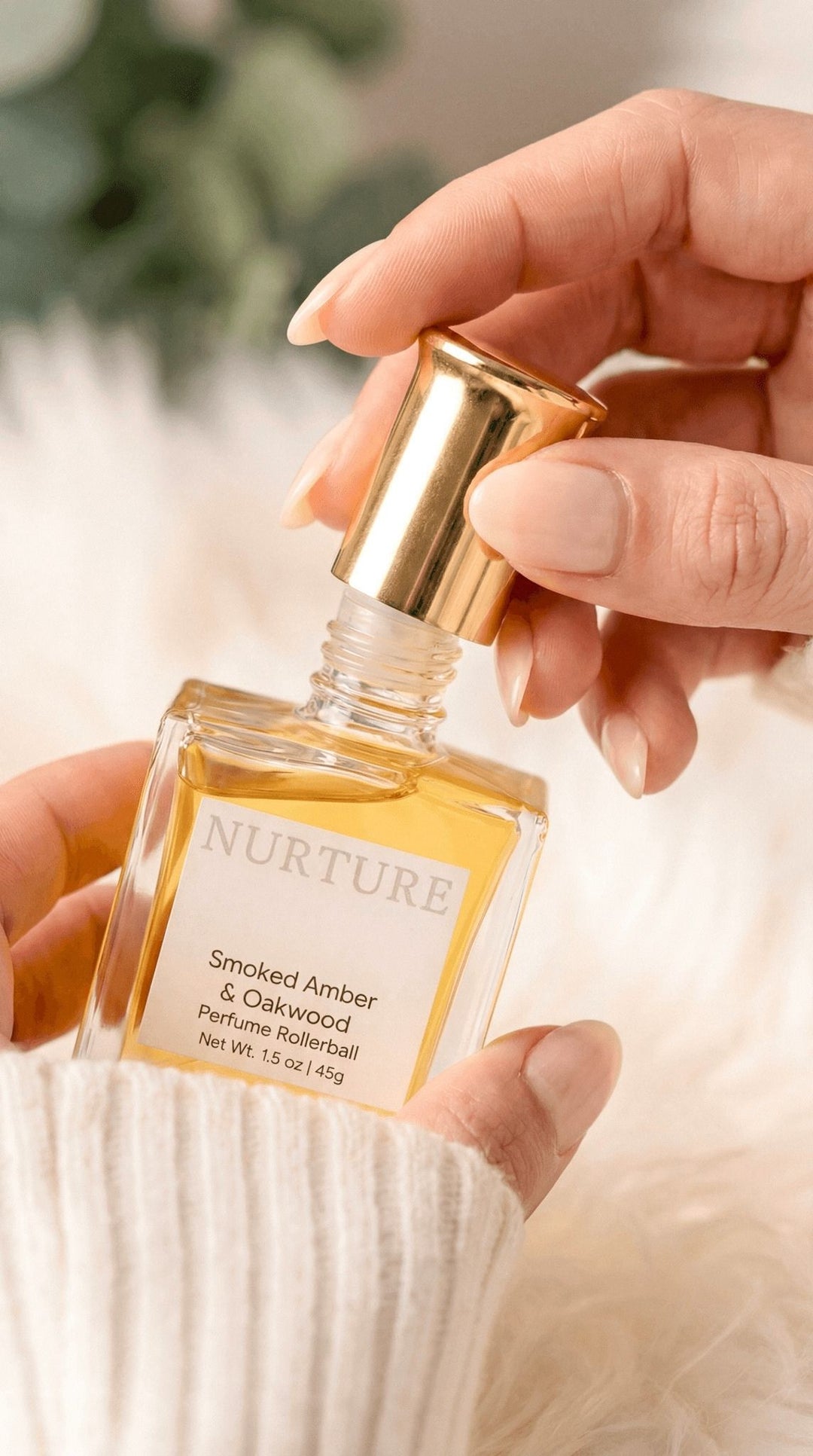 A woman's hand holding a bottle of Smoked Amber & Oakwood rollerball.