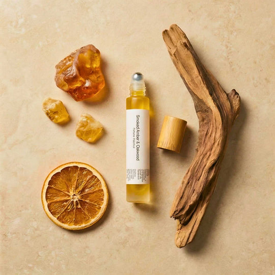 Smoked Amber &amp; Oakwood small rollerball on a neutral background with a piece of sandalwood and amber.