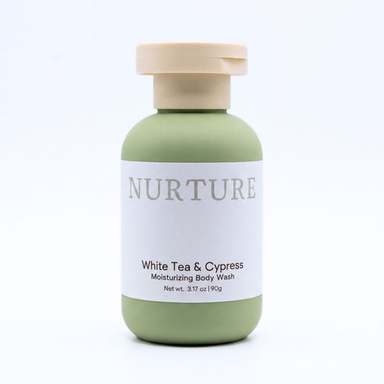 A bottle of NURTURE White Tea &amp; Cypress Moisturizing Body Wash, featuring a sage green bottle with a beige cap and a white label, set against a clean white background.