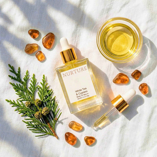 Nurture White Tea &amp; Cypress body oil with amber stones and greenery on a light background