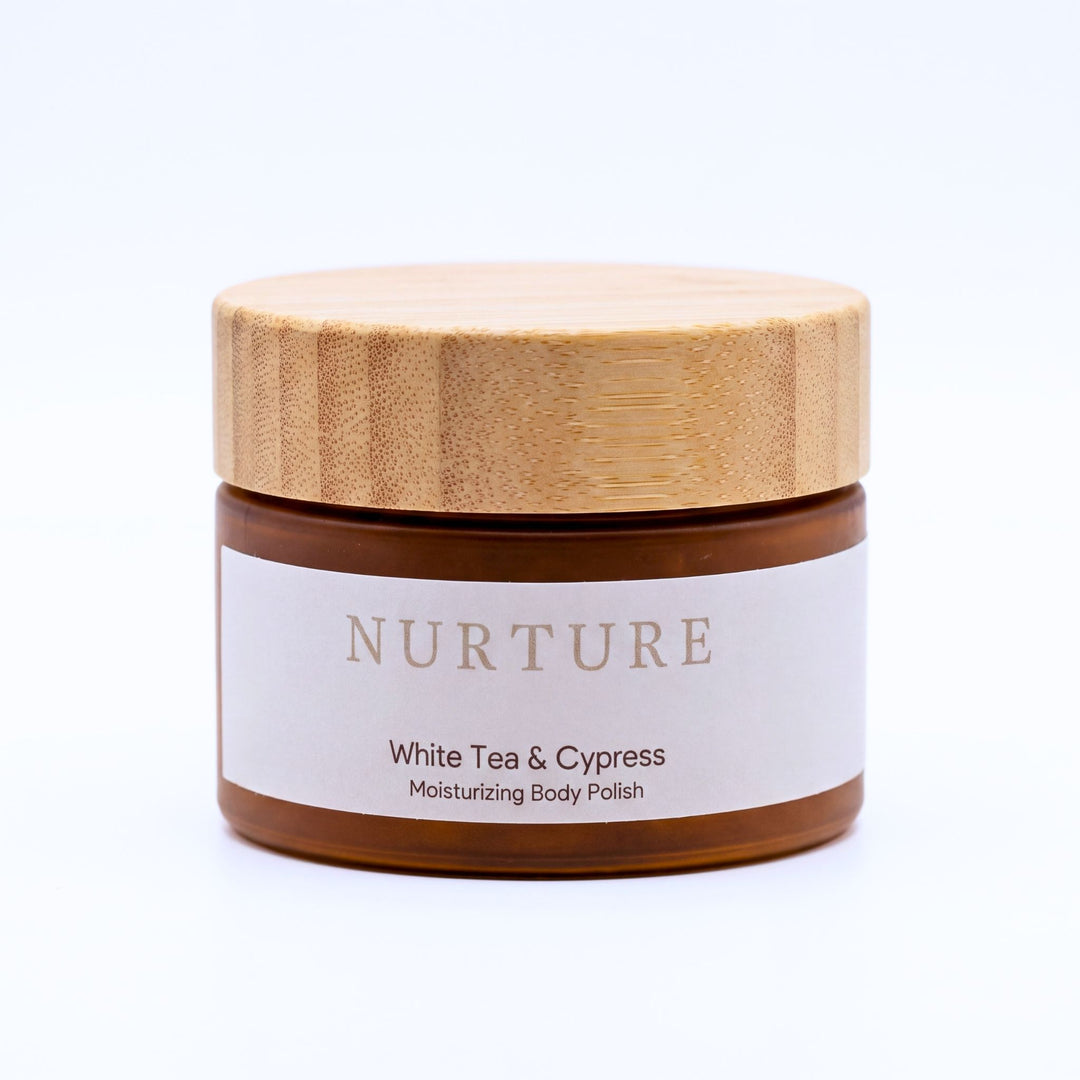 A jar of NURTURE White Tea & Cypress Moisturizing Body Polish with a light wood lid and a white label, set against a plain white background.