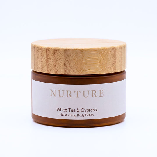 A jar of NURTURE White Tea &amp; Cypress Moisturizing Body Polish with a light wood lid and a white label, set against a plain white background.