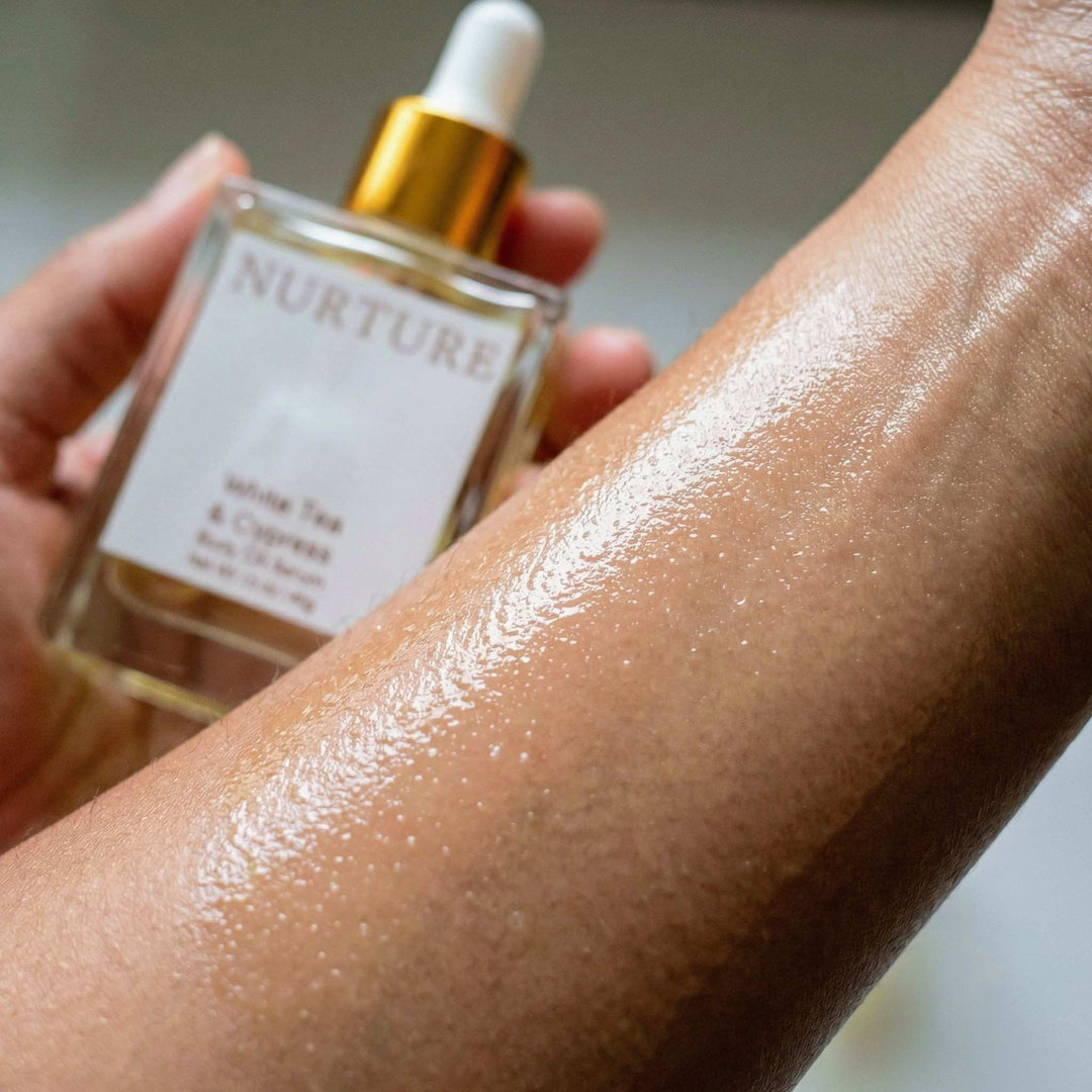 Hand holding White Tea &amp; Cypress body oil above a person&