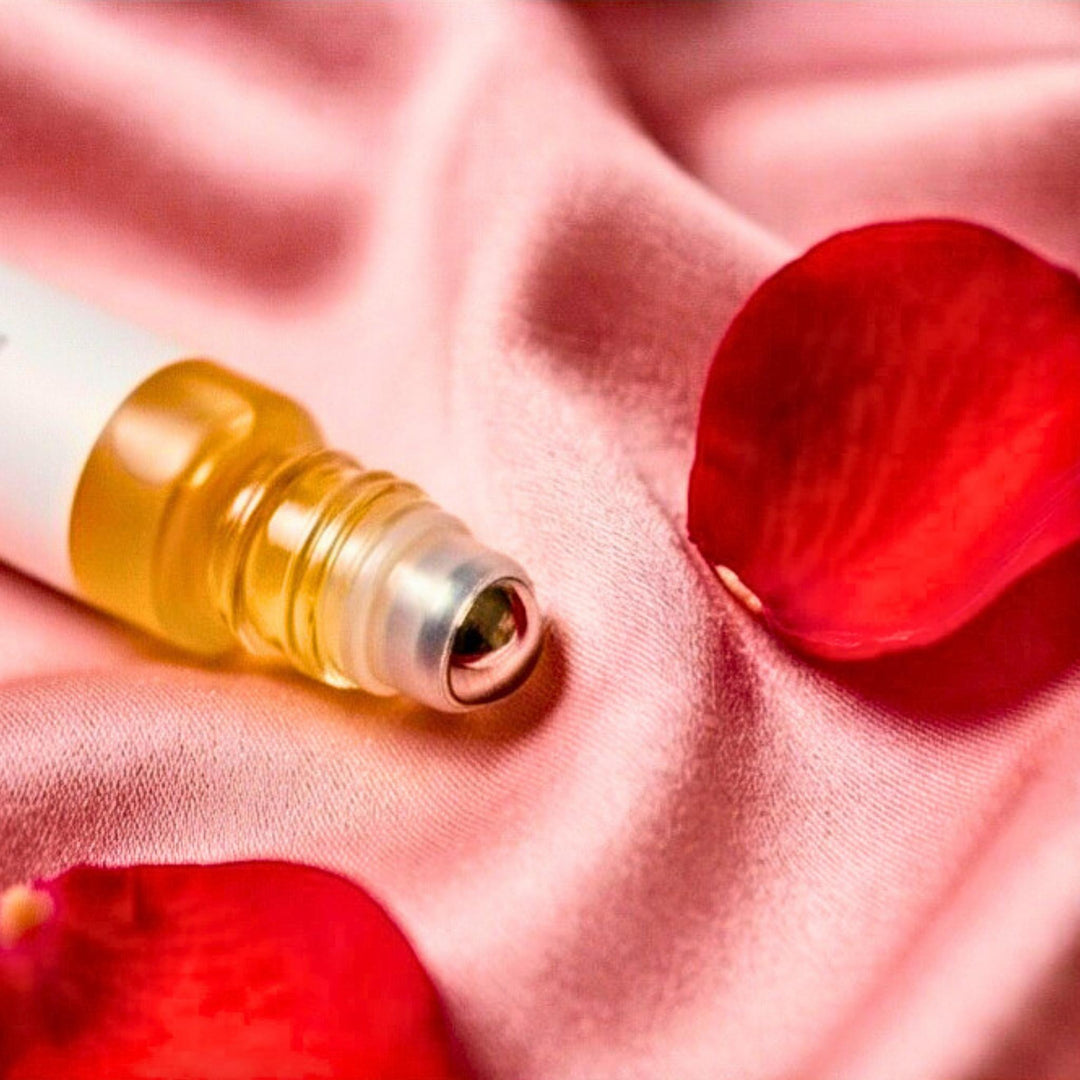 Black Rose Santal small rollerball on pink fabric next to rose petals.