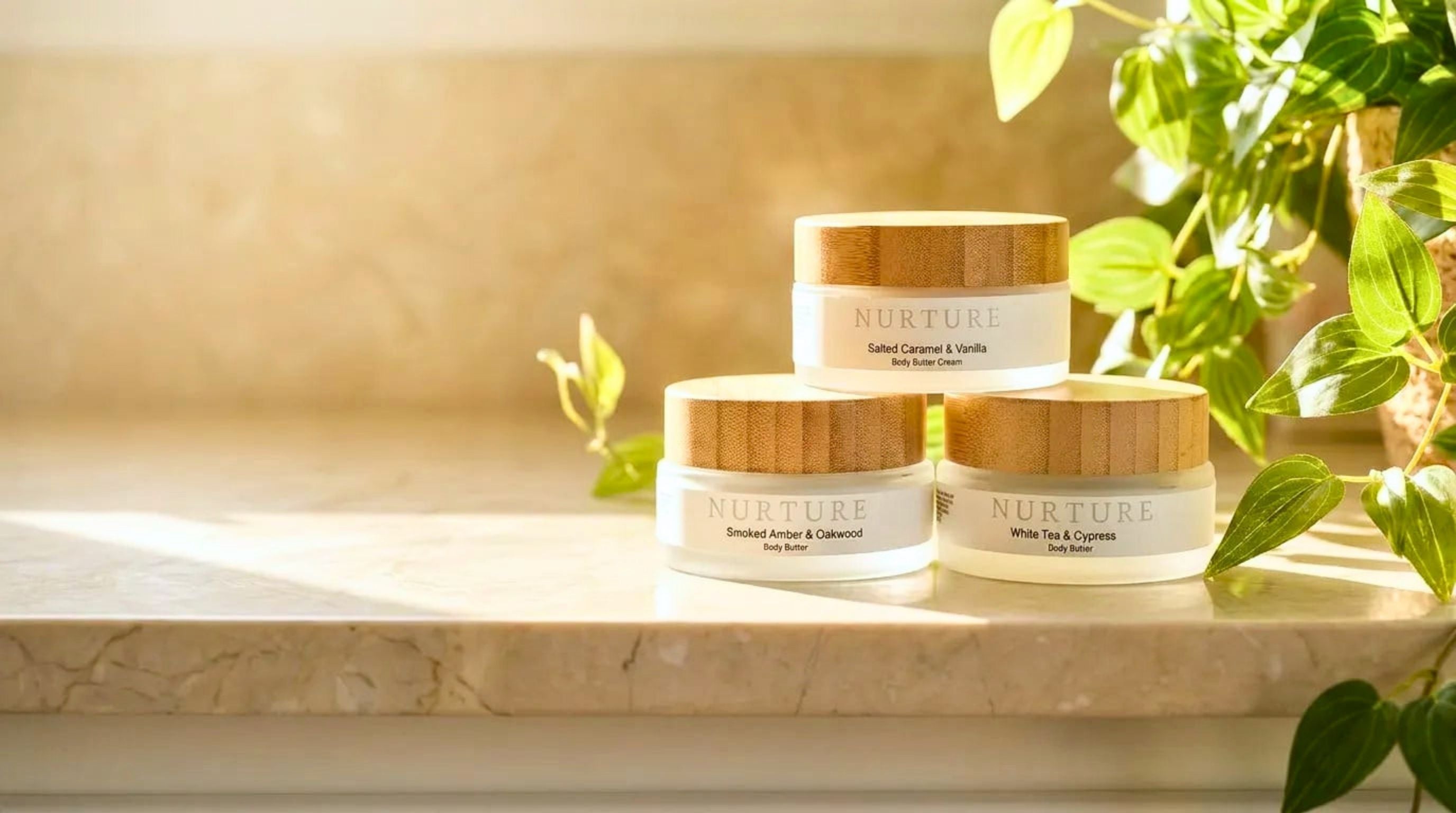 Three jars of 'Nurture' cream on a marble surface with greenery in the background