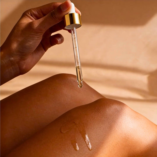 Hand holding a dropper of body oil with a beige background