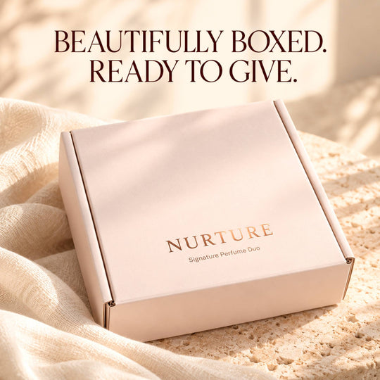 A pale blush pink box with the brand name NURTURE printed in rose-gold foil, resting on a textured beige surface with draped fabric. The text &