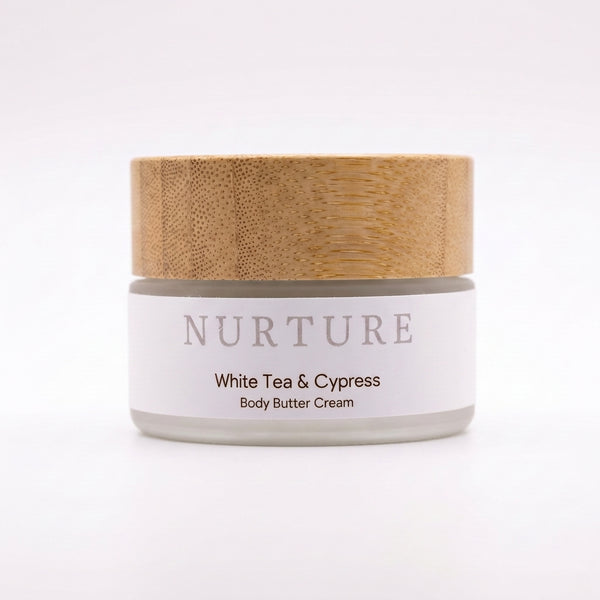 Body butter cream jar with wooden lid labeled 'Nurture White Tea & Cypress' on a white background